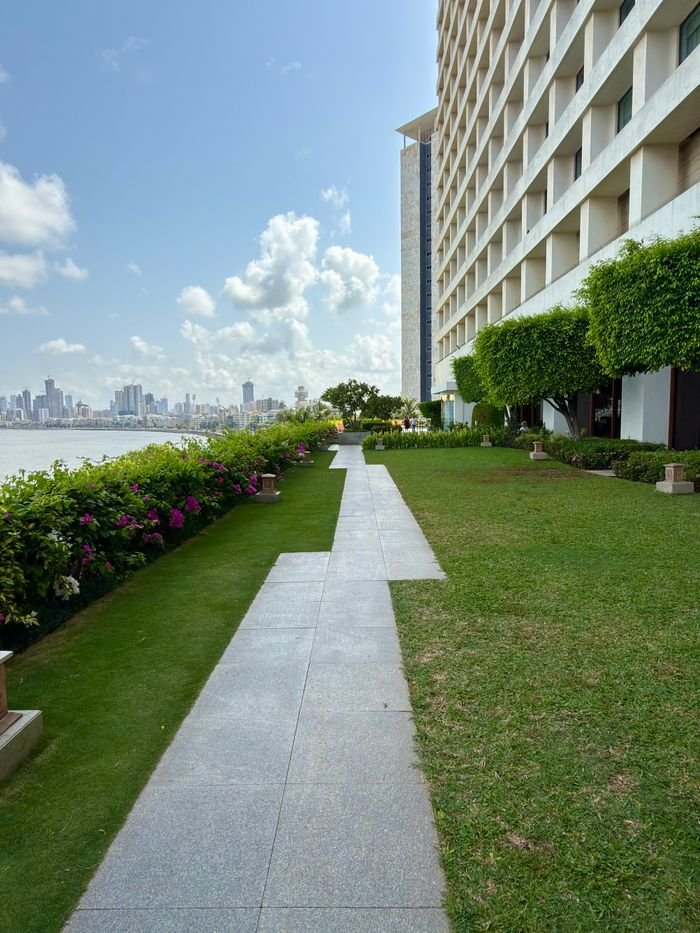 Beautiful garden pathway along a waterfront with a cityscape view under a clear blue sky.